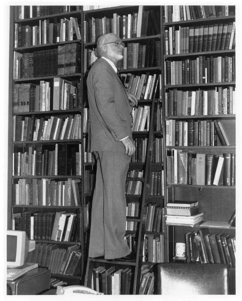 Frank Carver standing on a rolling ladder in his personal library, reaching toward the shelves.